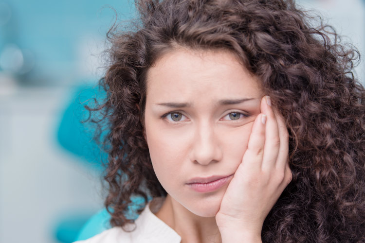 Curly haired brunette woman holding her face due to tooth pain