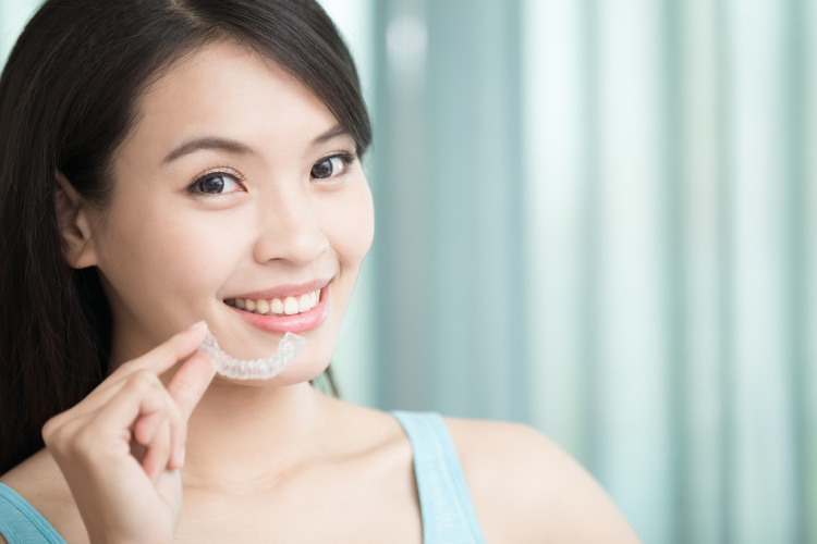 Dark haired smiling girl shows her Invisalign clear aligner